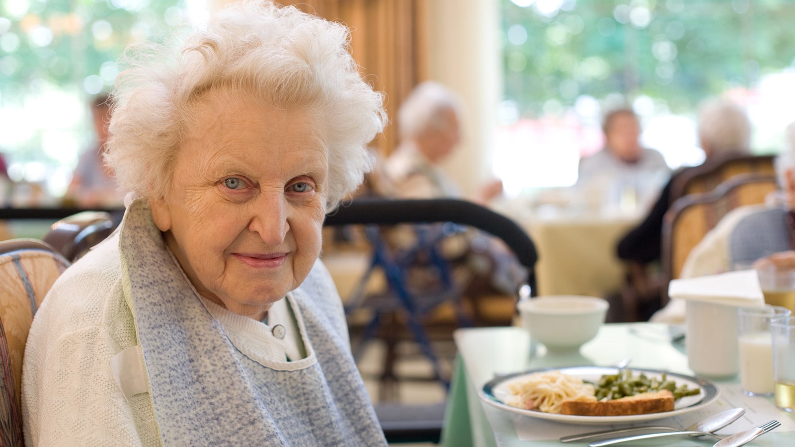 Senior woman with white hair wearing bib at dinner table