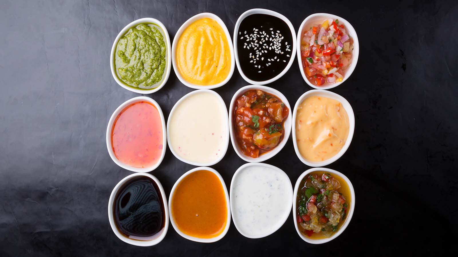A variety of sauces in white bowls against a black background
