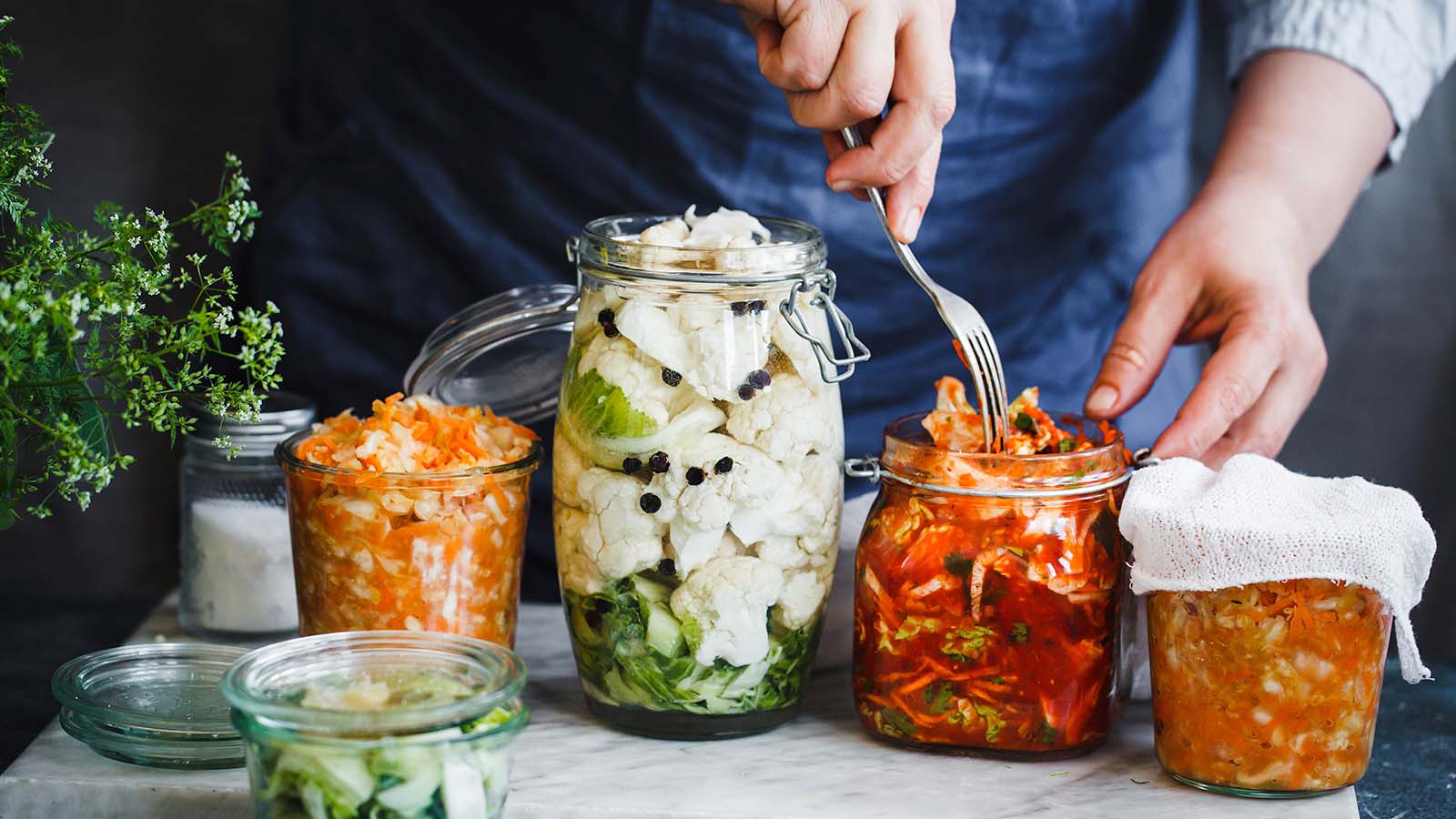 Cook with fork standing in front of jars of fermented preserved vegetarian food