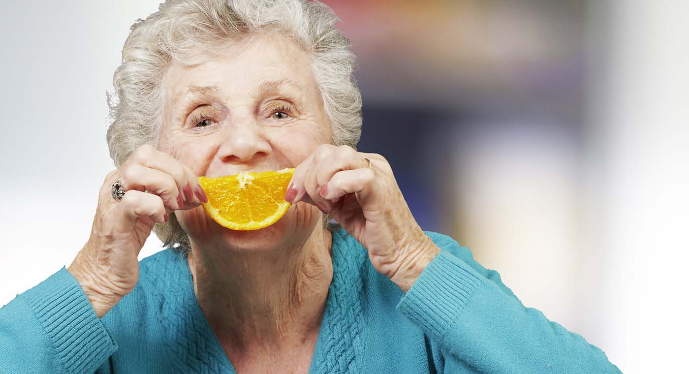 senior woman in blue holding up an orange slice to her face