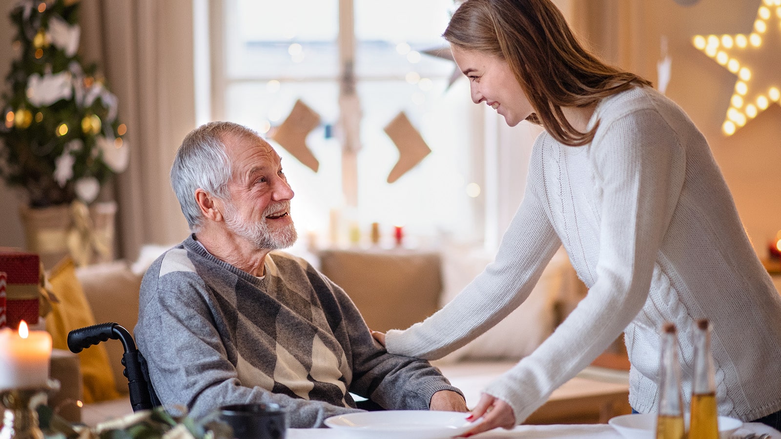 Younng woman with white sweater serving senior man in wheelchair