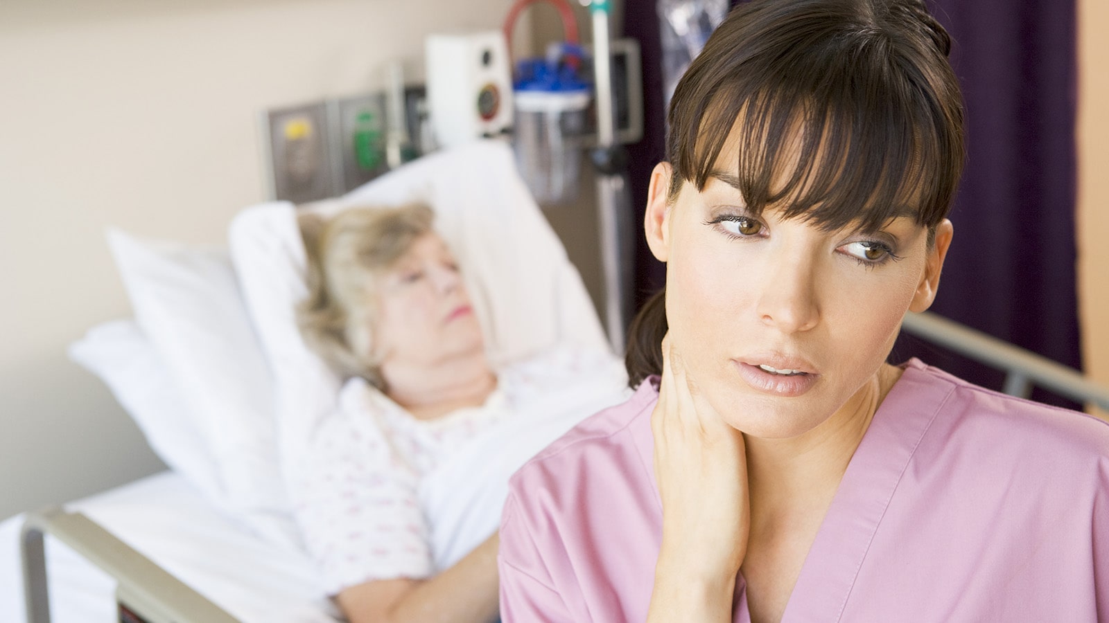 Nurse wearing pink with hand on her neck looking distraught