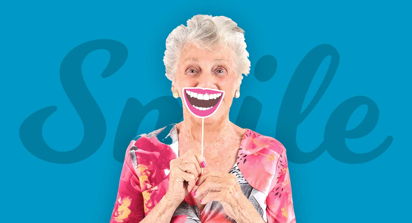 senior woman in floral shirt holding up a smile prop