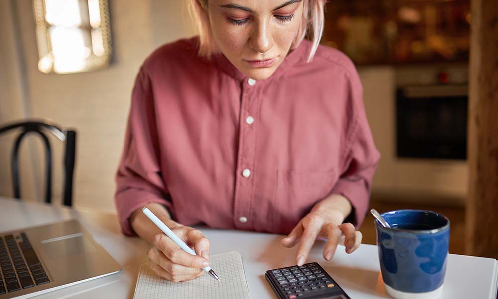 Woman in pink shirt using a calculator and holding pen