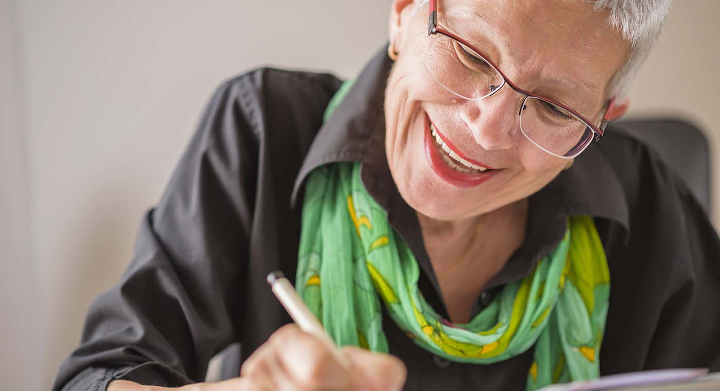 senior woman wearing glasses smiling while writing in book