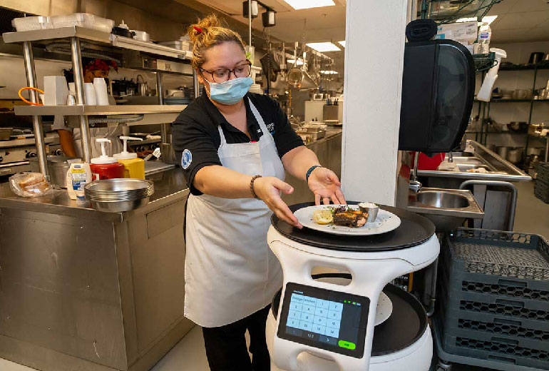 chef wearing a covid mask placeing meal on a food delivery robot