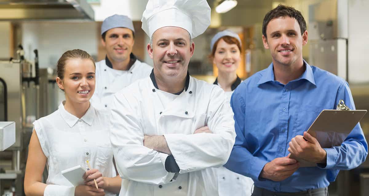 Chef in white standing with kitchen staff looking at camera