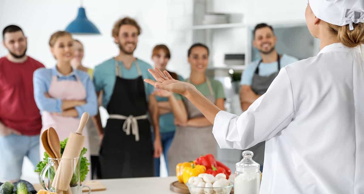 Chef in white standing with kitchen staff looking at camera