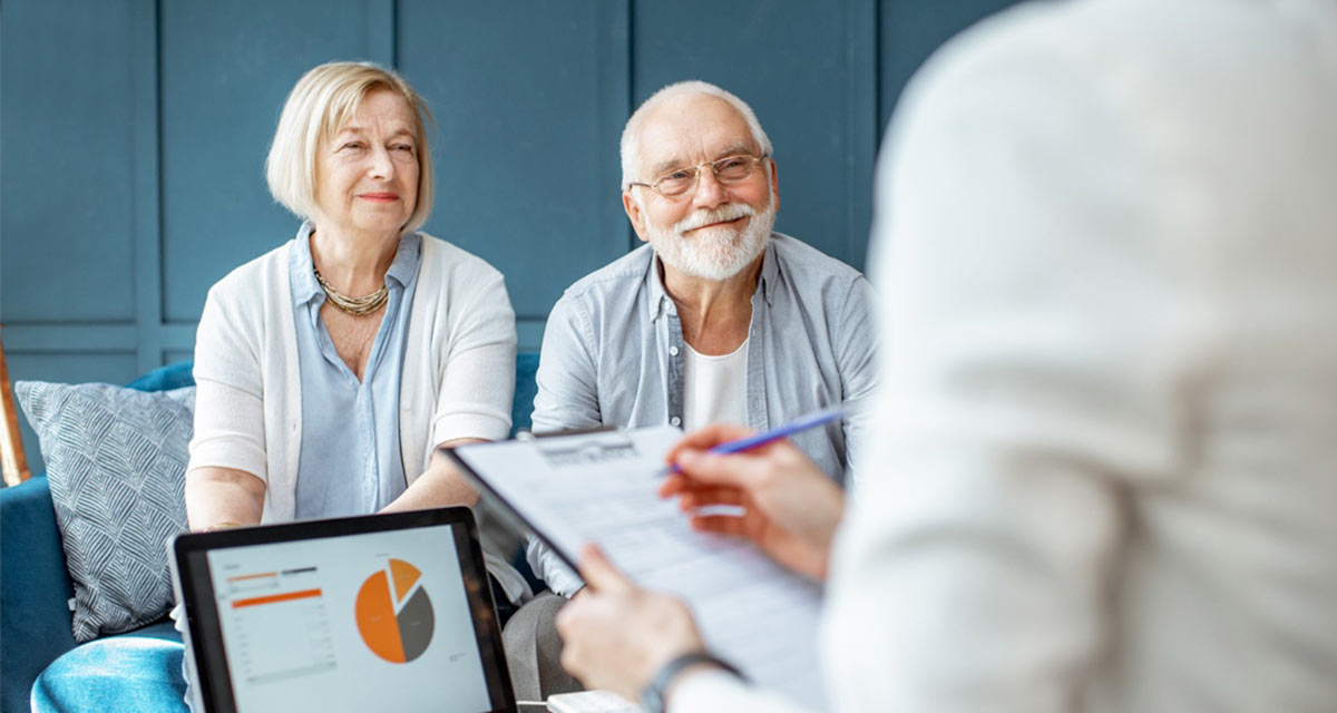 Older couple smiling while being evaluated by consultant with laptop