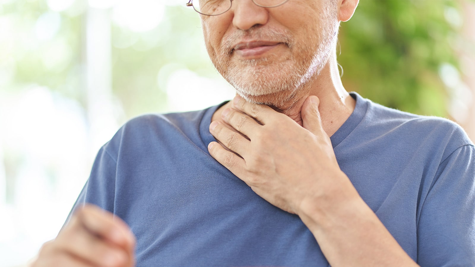Elderly man in blue shirt holding his throat