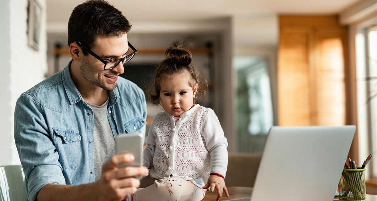 Father in blue shirt showing his young daughter his cellphone and computer