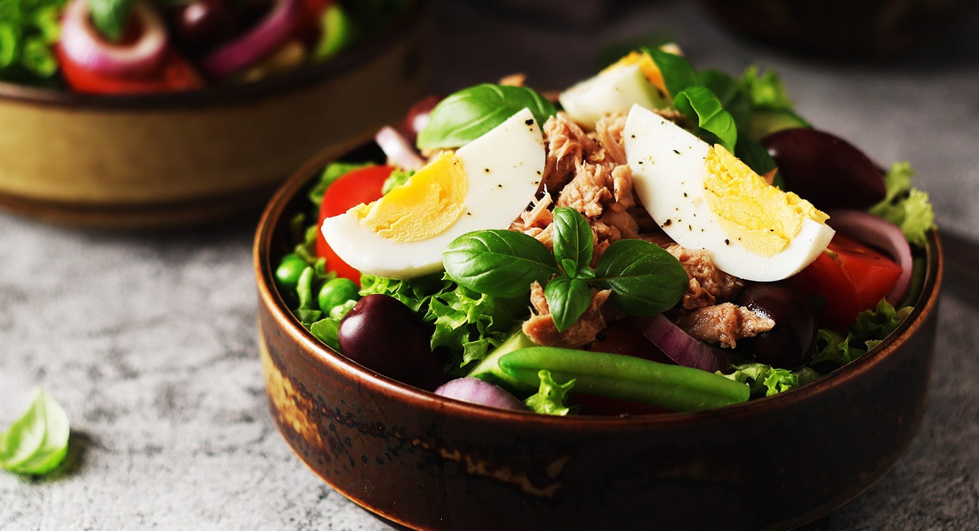 Salad in bowl with eggs, olives, tomatoes, lettuce