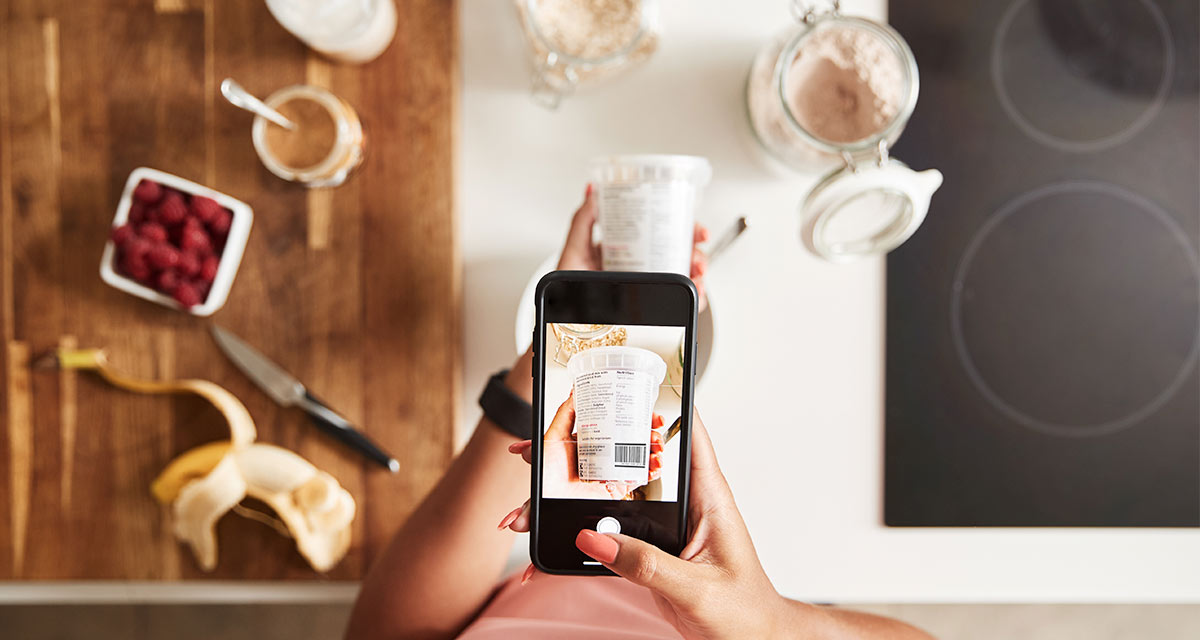 Woman looking down at her cellphone taking picture of yogurt cup