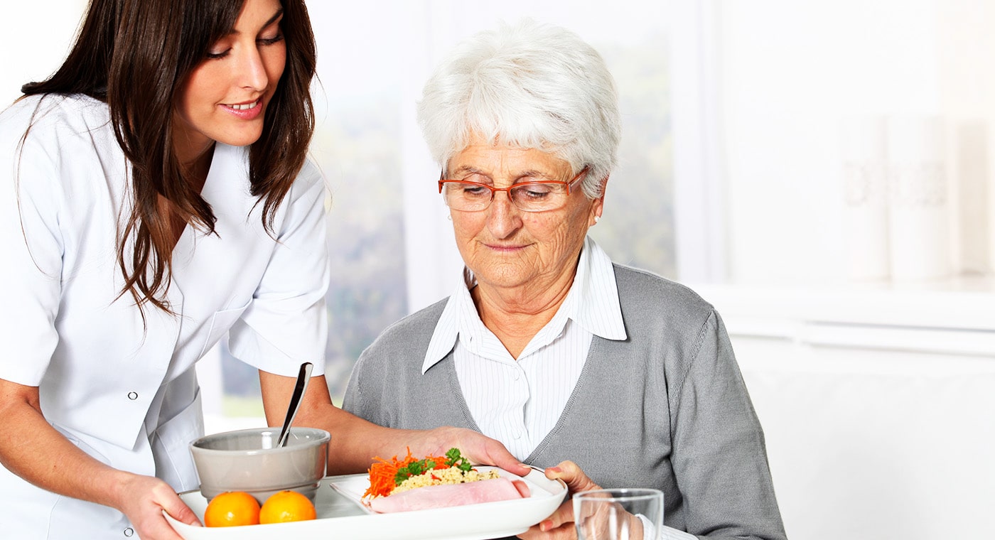 Nurse serving tray meal to senior woman