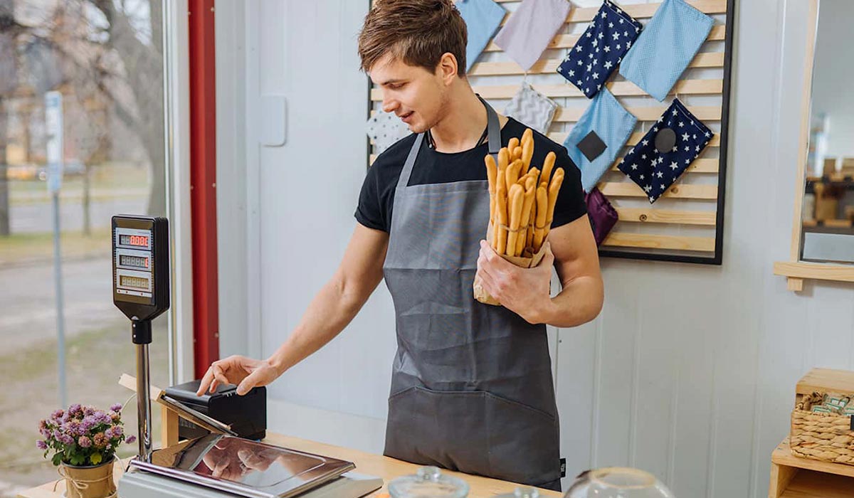Young man waring apron holding breadsticks using a point of sale system