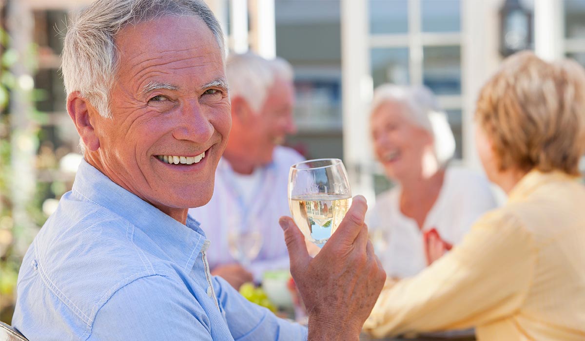 Older man wearing a blue shirt at dinner with friends smiling while holding a glass