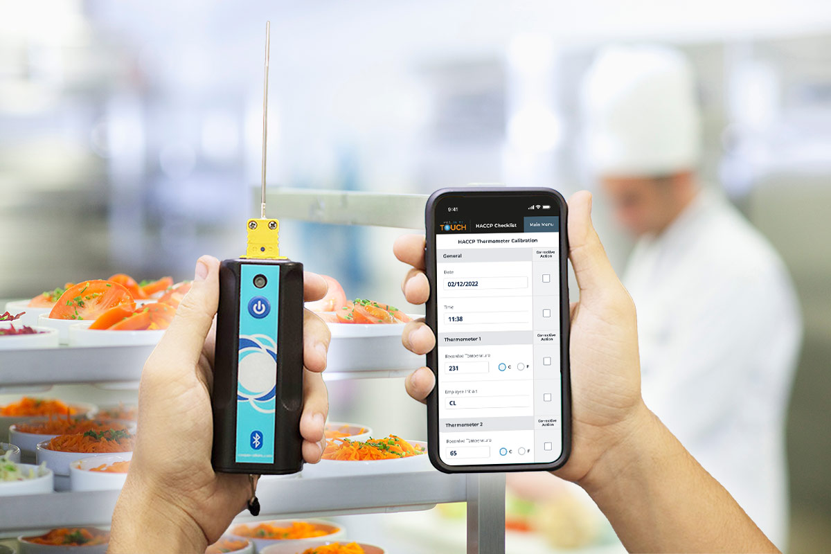 Hands holding Cooper Atkins Blue2 wireless thermometers in front of food table