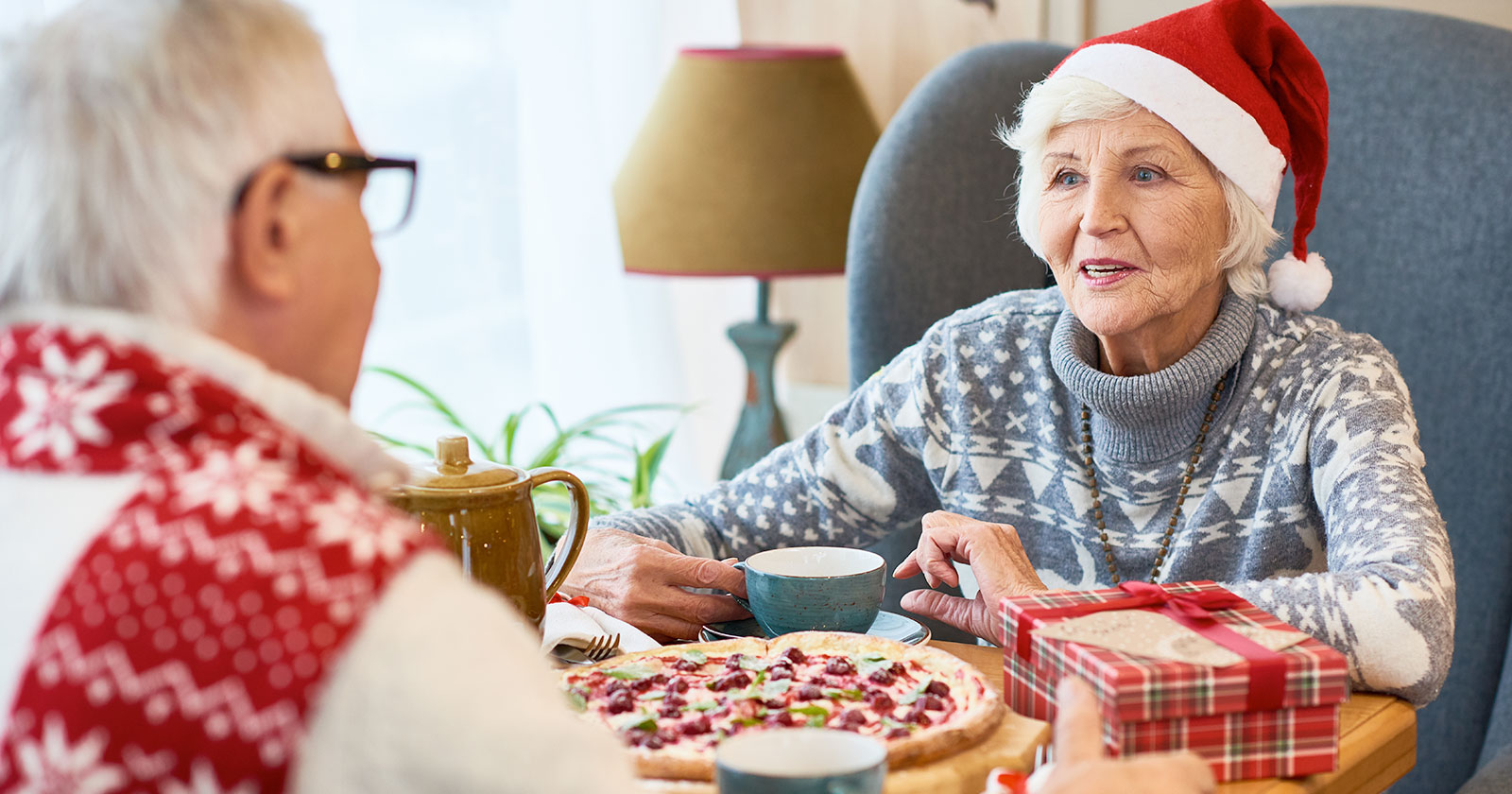 Elderly couple wearing Christmas sweaters sitting at dinner table together having a conversation