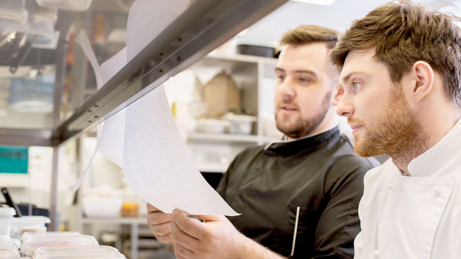 Chef and cook looking at meal orders in kitchen