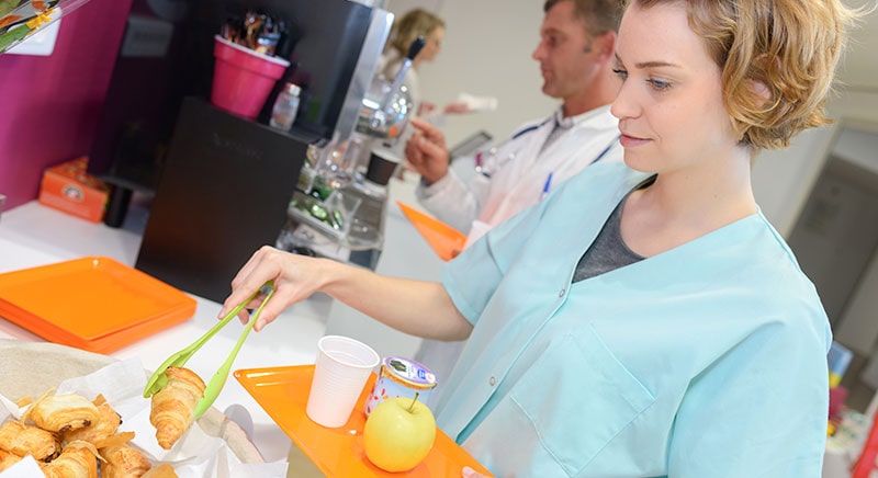 Female nurse wearing blue taking a croissant with tongs