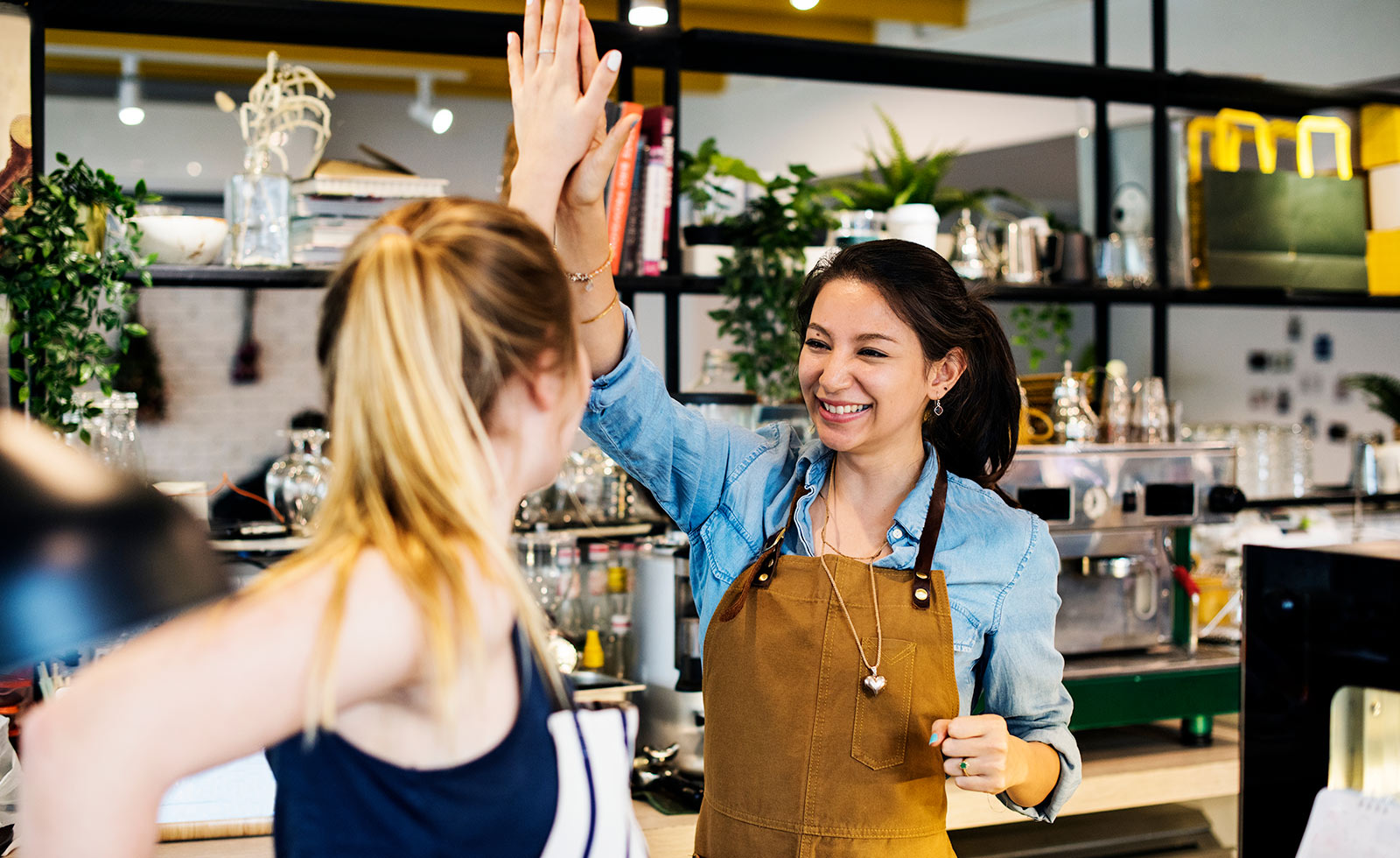 Two women wearing aprons giving each other high five in cafe