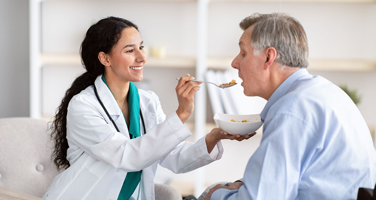 Smiling female nurse in white feeding senior male resident