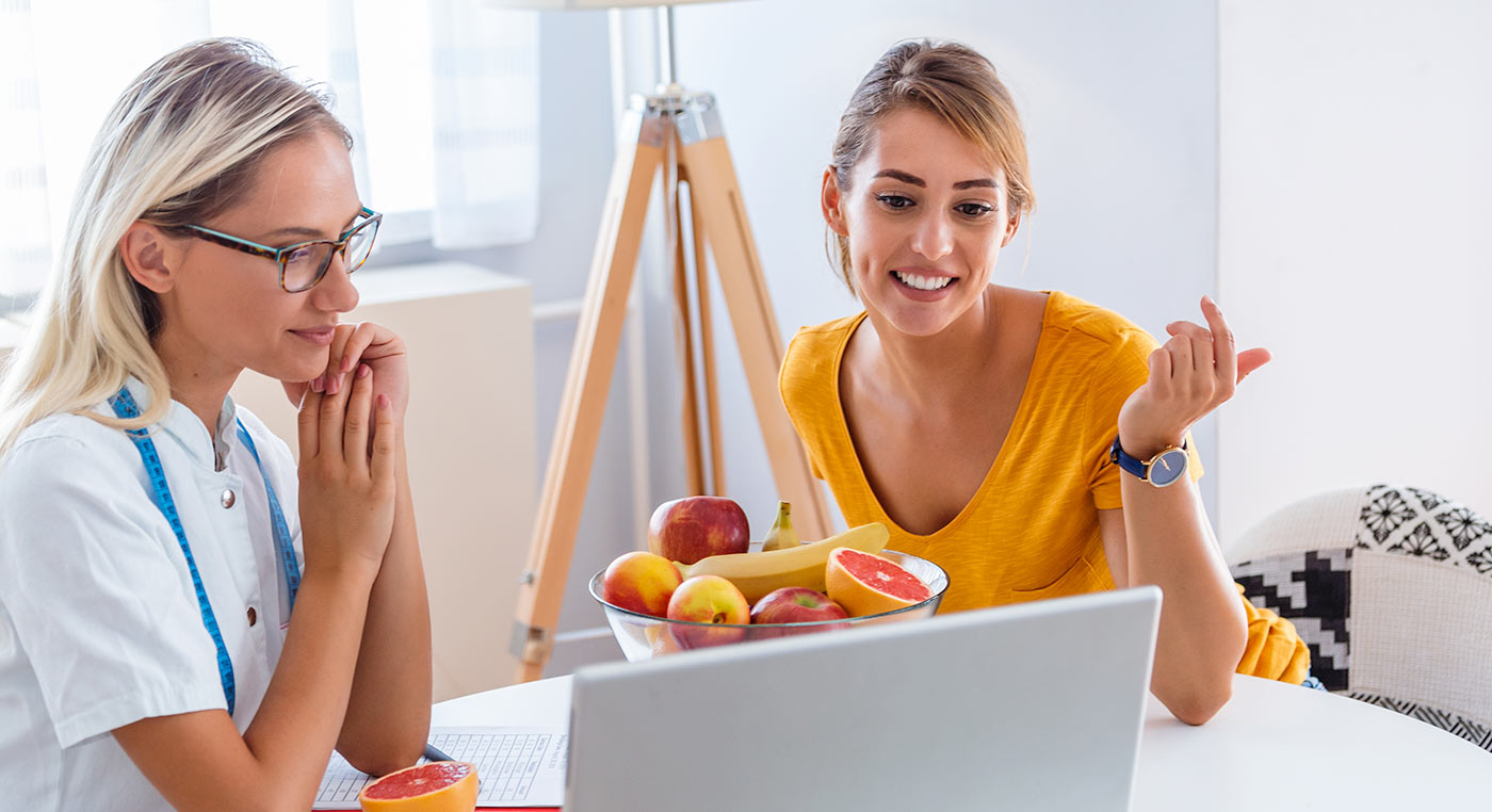 Two femail dietitians looking at laptop with fruit bowl