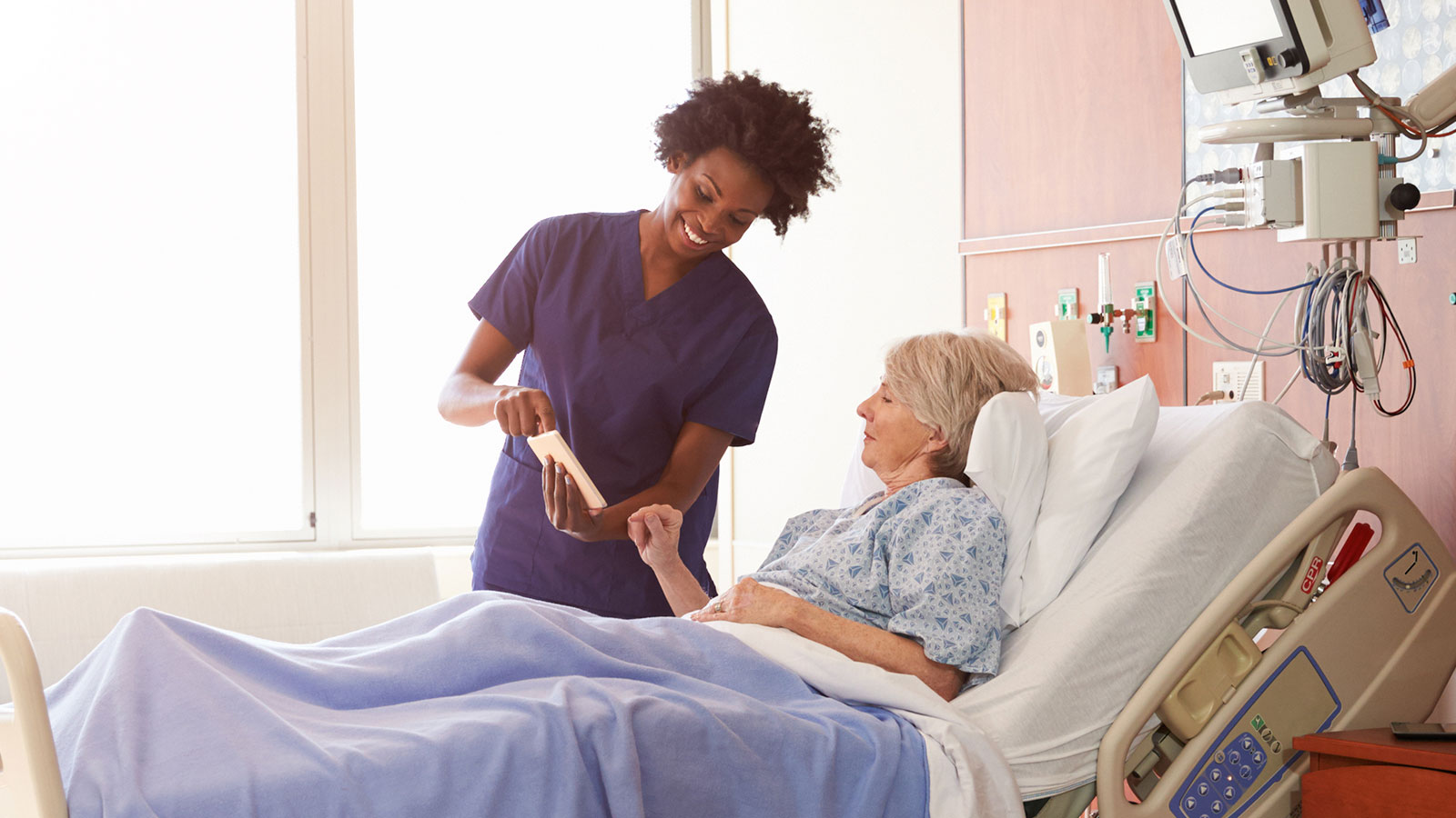 African american nurse showing tablet screen to caucasian female patient in hospital