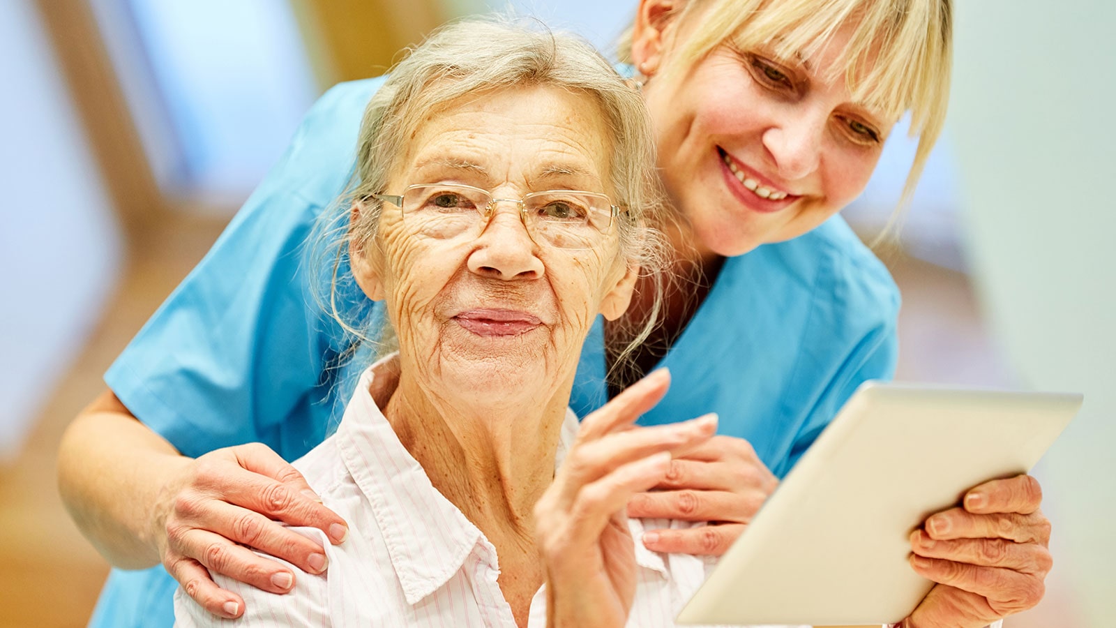 Nurse wearing blue with hand on residence shoulder looking at a tablet