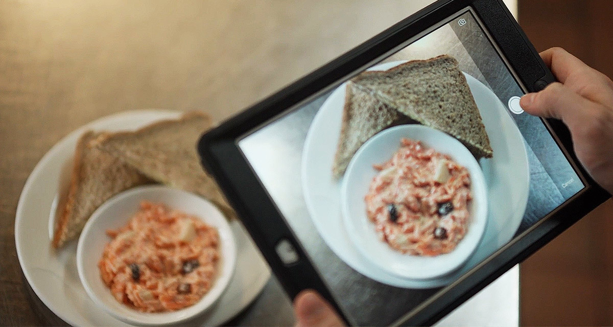 Woman holding a tablet while taking picture of food