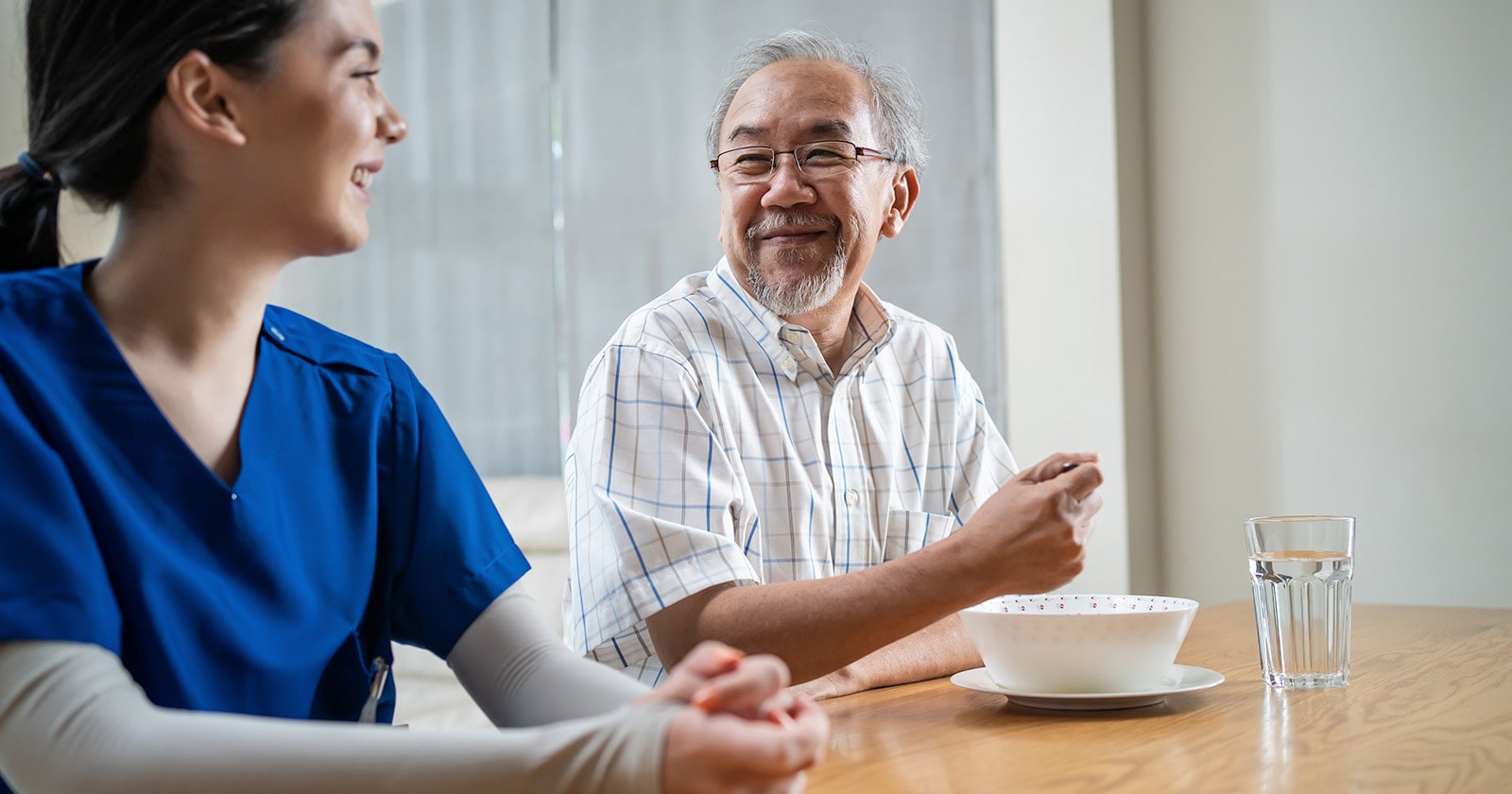 Older asian man wearing white smiling at nurse wearing blue