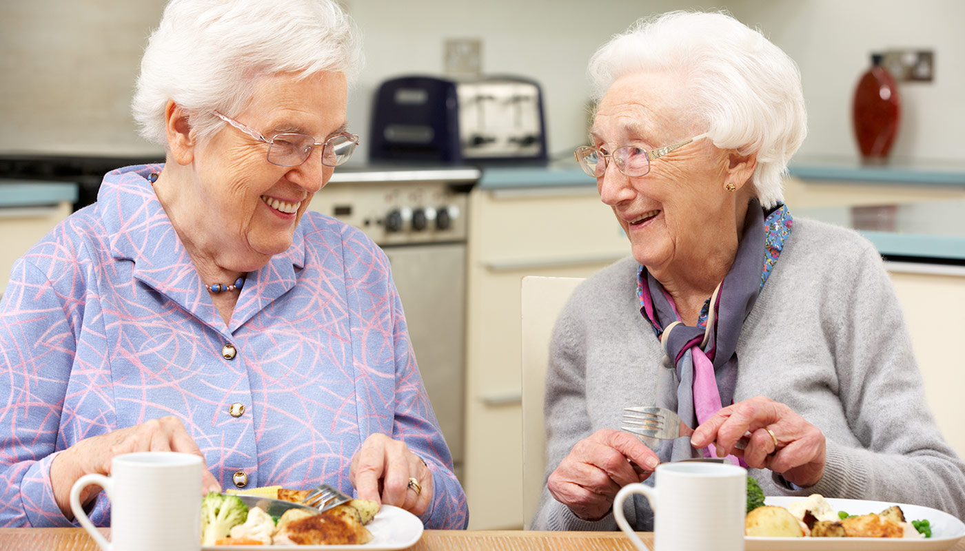 Senior womean with white hair and glasses sharing a laugh while eating meal