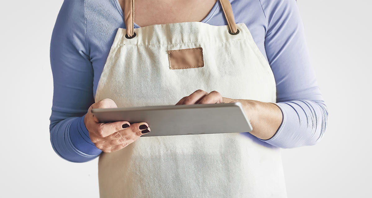 Woman with blue shirt in apron working on a tablet with white background