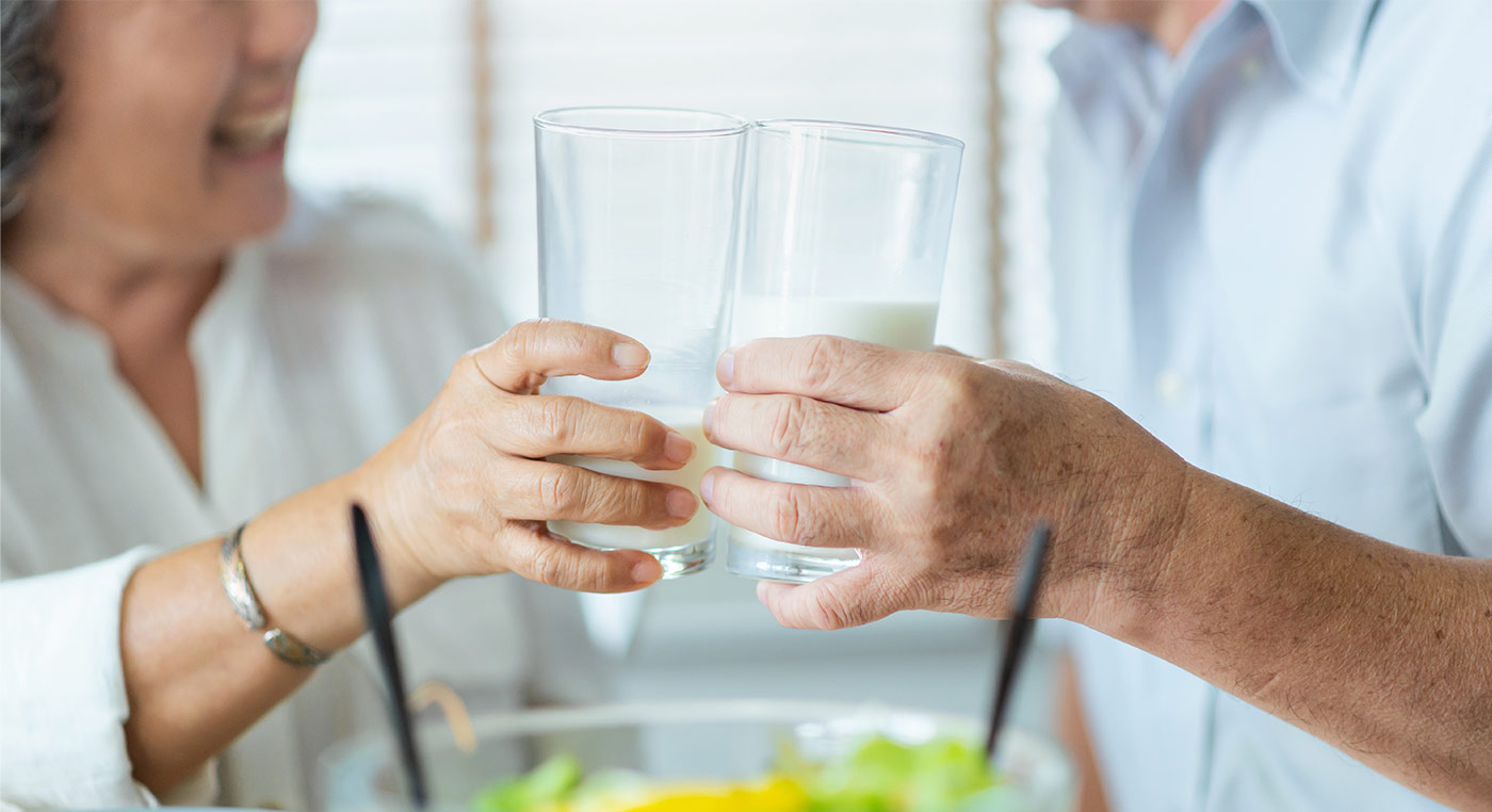 Smiling Asian senior man and woman holding glasses of milk. 