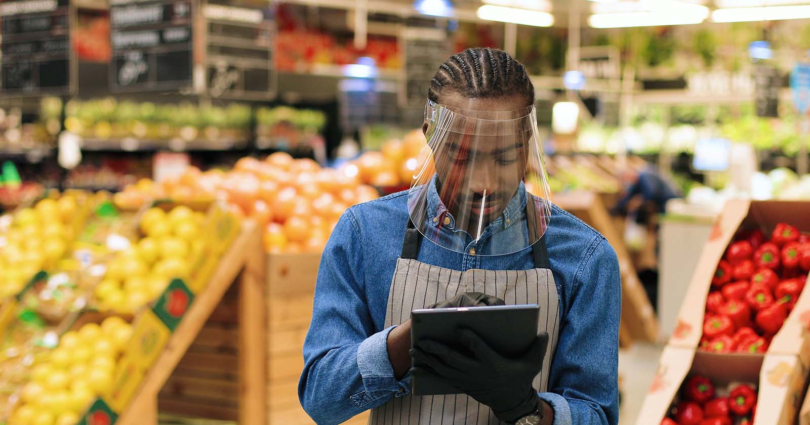 African american grocery clerk wearing a covid mask using tablet in produce department