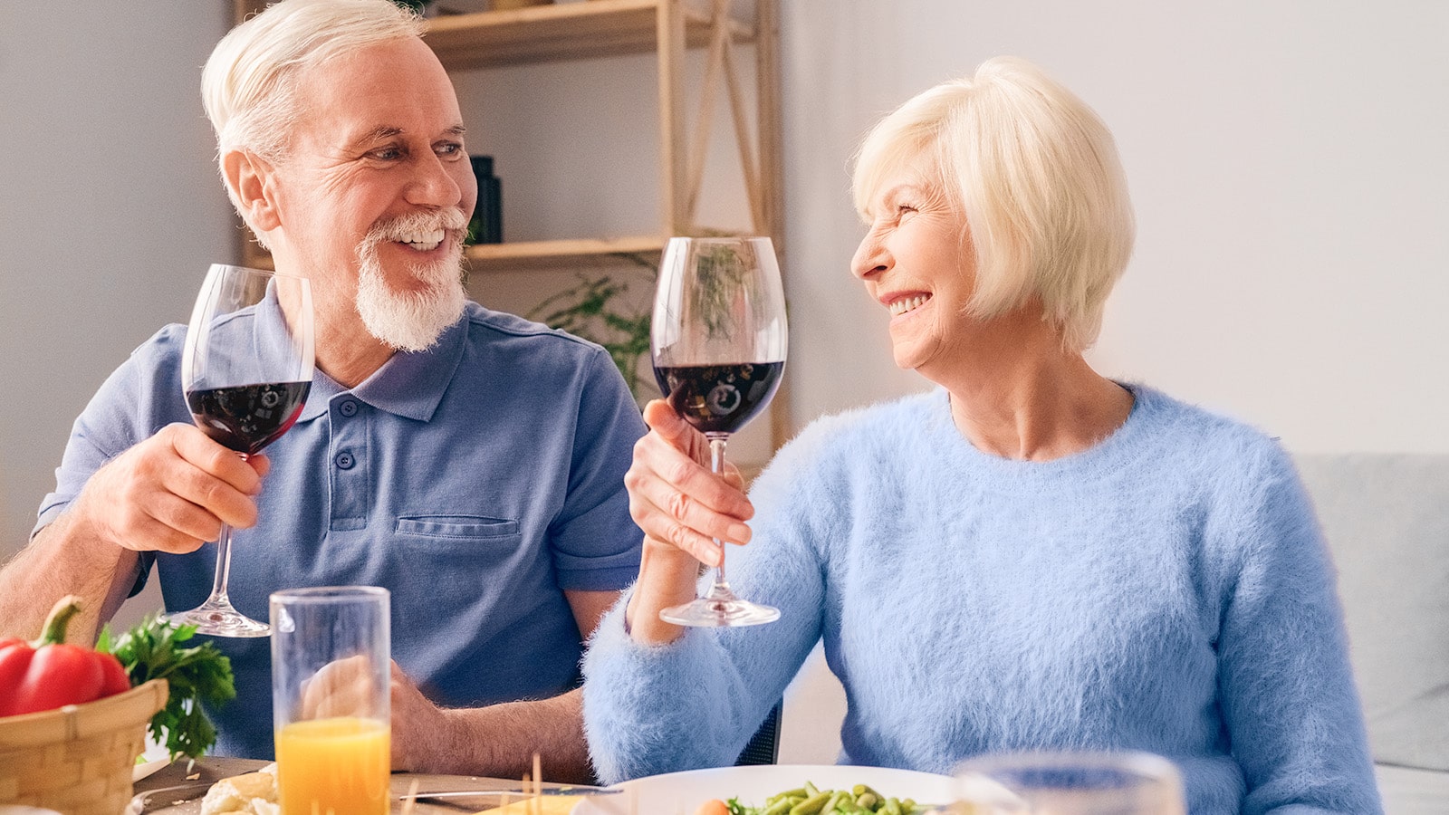 Senior woman and man wearing blue holding up wine glasses at dinner