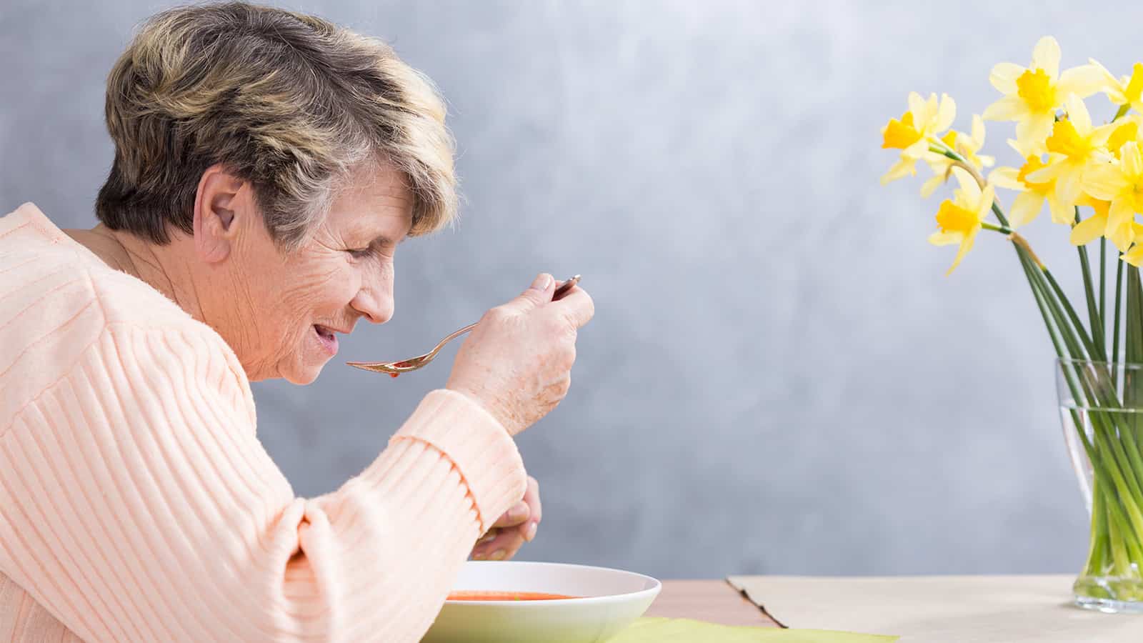 Elderly woman wearing pink smiling while eating soup