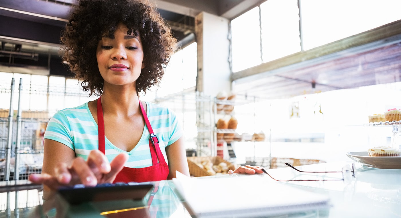 African american woman wearing red apron operating a calculator