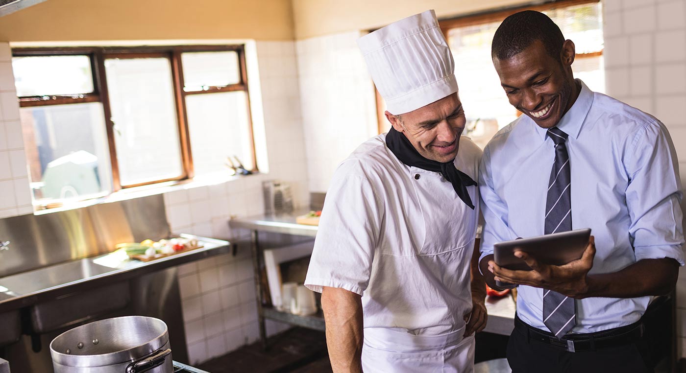 Kitchen manager in tie looking at tablet with head chef in kitchen