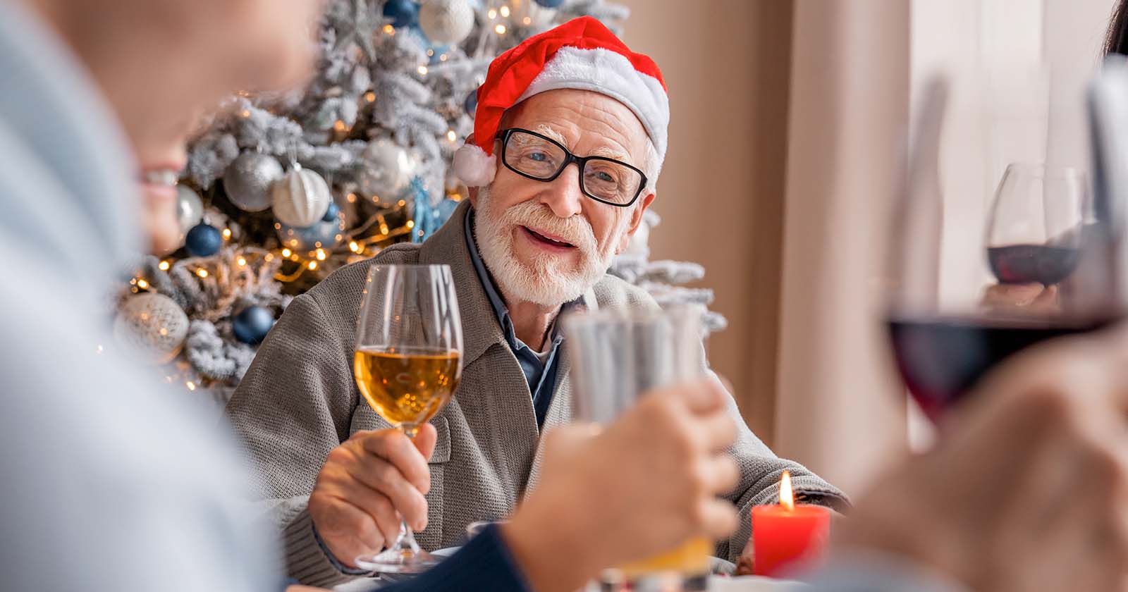 Elderly man wearing santa hat holding glass of champagne