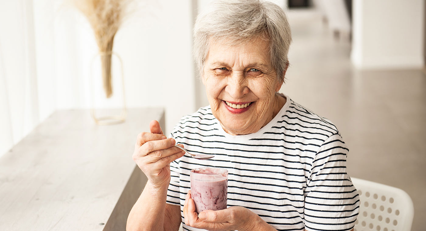 Senior woman in striped shirt smiling while eating strawberry yogurt