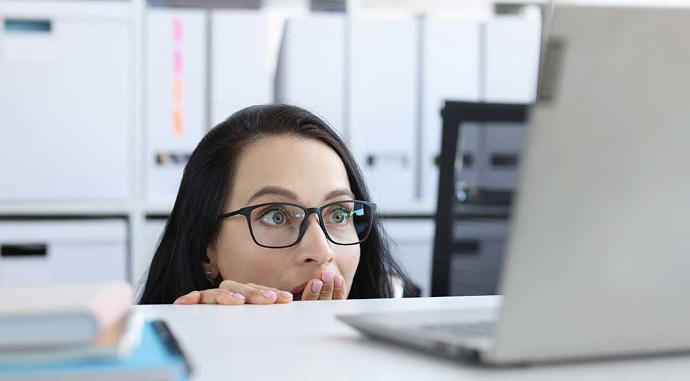 Woman in glasses surprised while looking at laptop